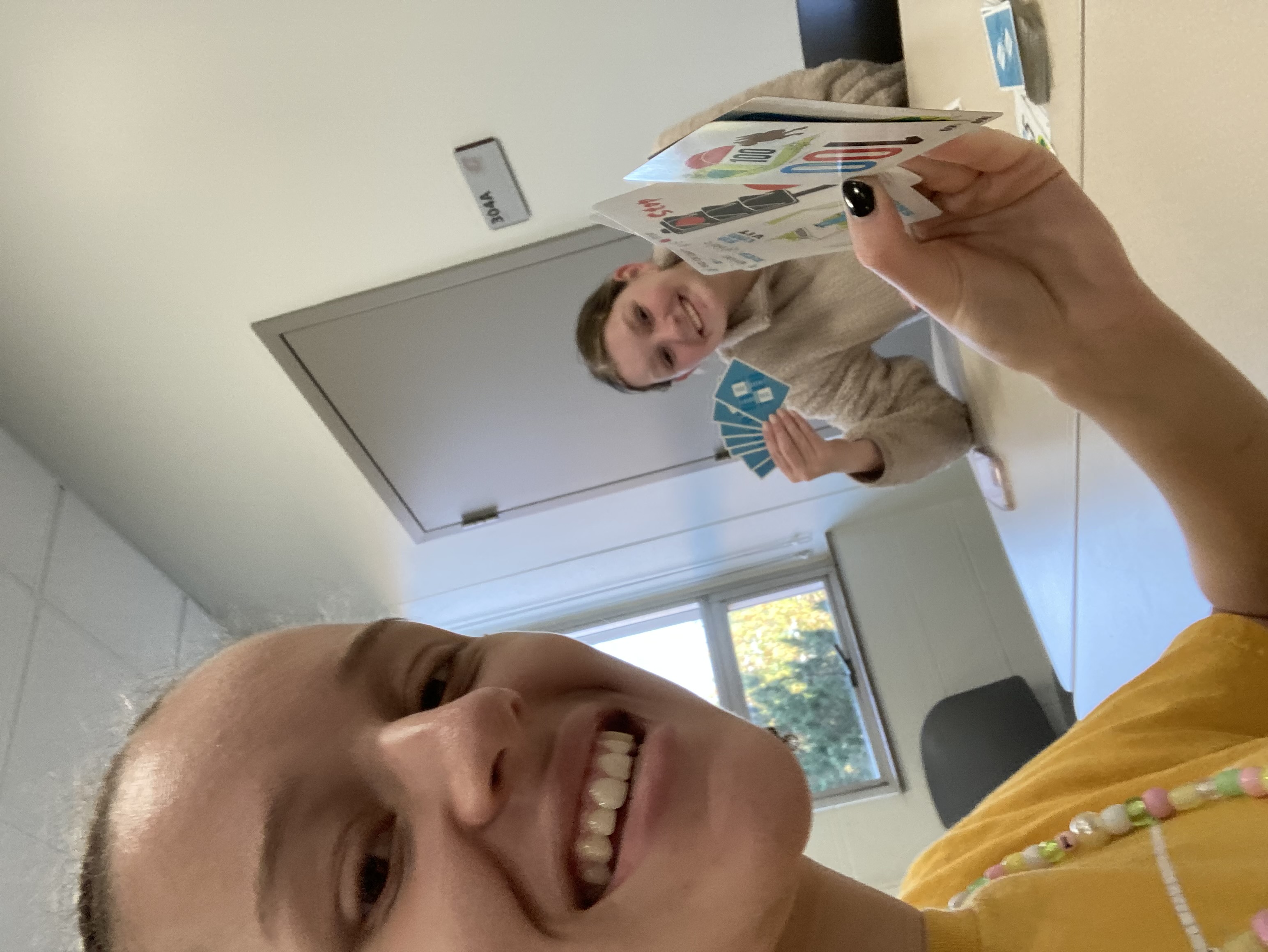 Selfie of Gabrielle holding Mille Bournes cards with Dahkota in the Background